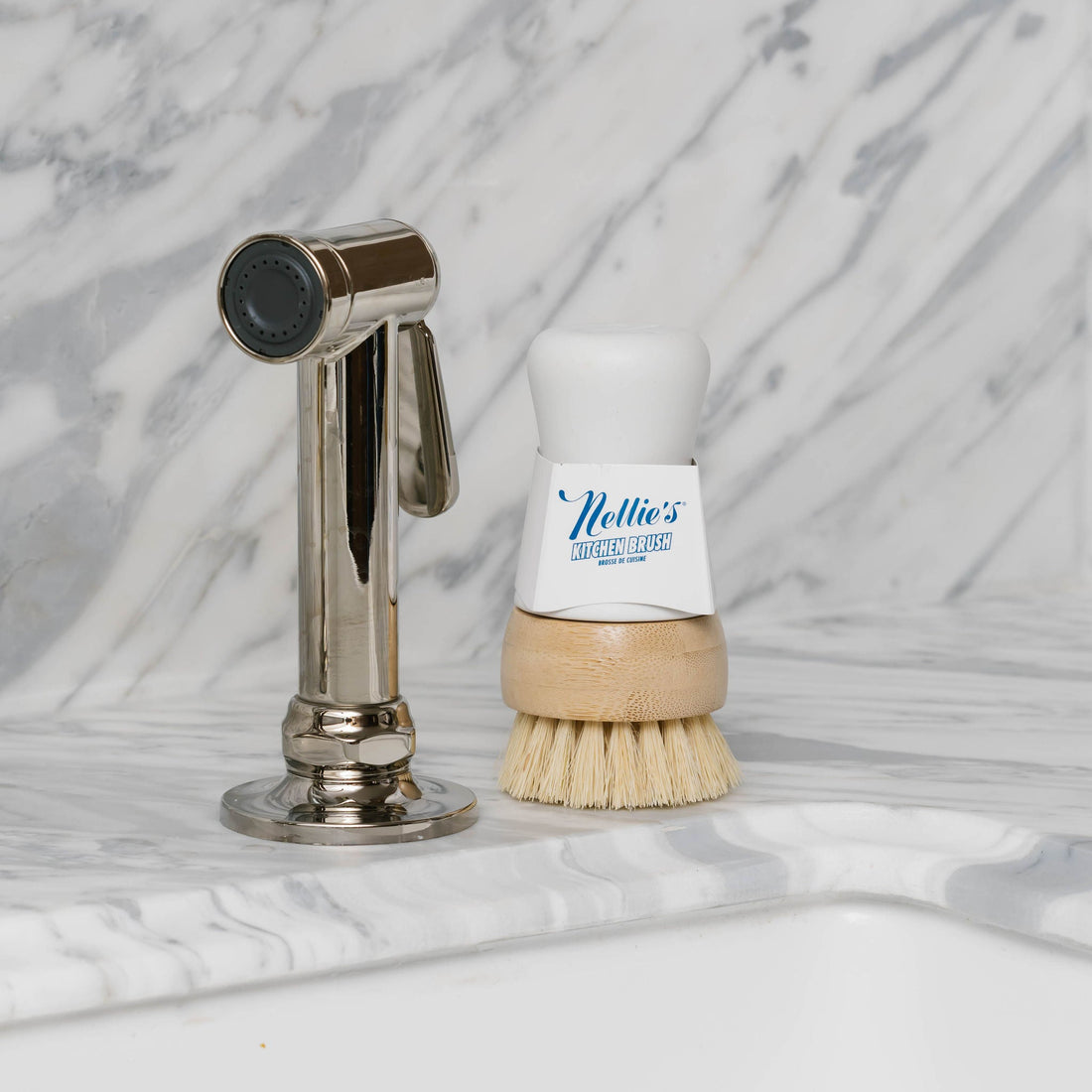 Nellie's Kitchen Brush with a bottle of cleaning solution next to a spray nozzle on a marble countertop.
