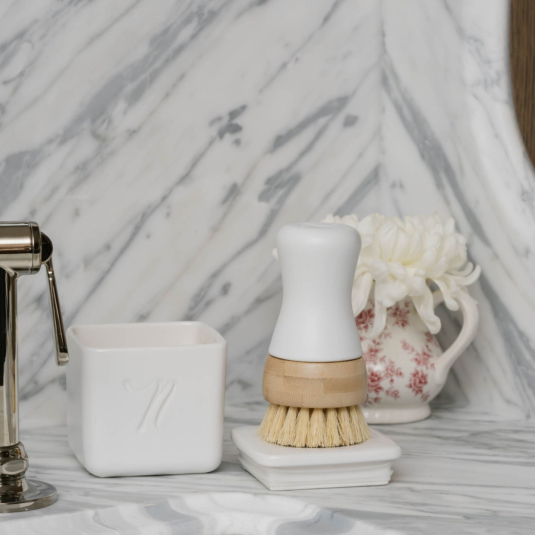 Bathroom sink area with a scrubbing brush, soap dish, and decorative items on a marble countertop.