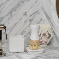 Bathroom sink area with a scrubbing brush, soap dish, and decorative items on a marble countertop.