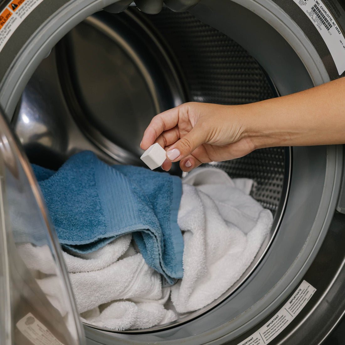 Hand placing a laundry detergent cube into a washing machine with clothes inside