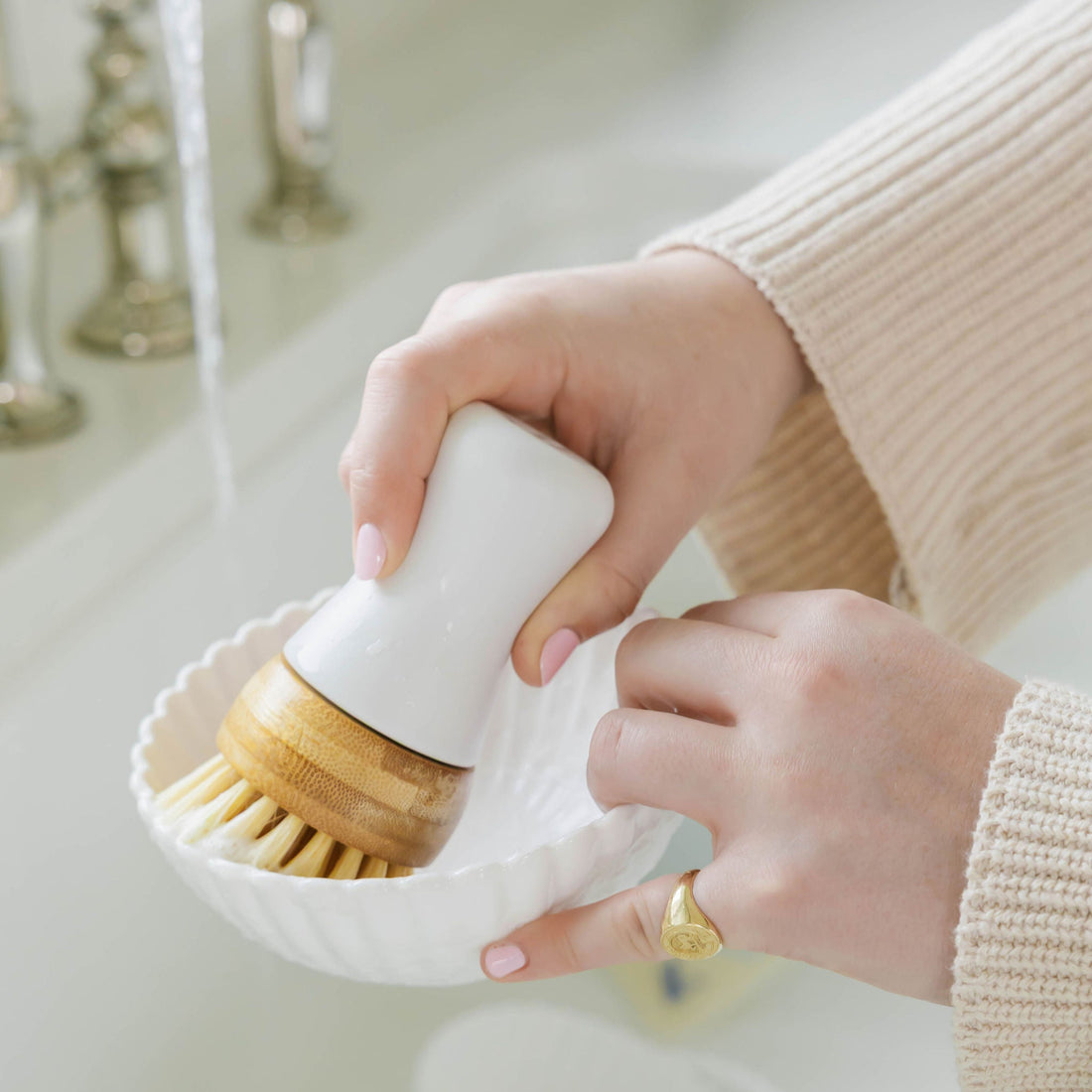 A close-up of a person's hands using Nellie's Kitchen Brush under running water in a sink.